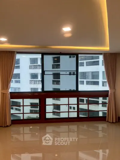 Spacious living room with large windows offering city views in modern apartment.