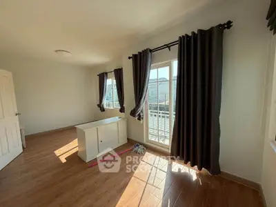 Spacious sunlit room with wooden flooring and large windows opening to a balcony.
