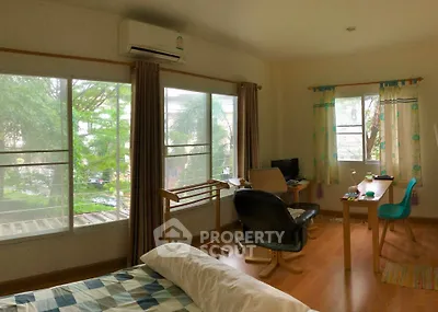 Cozy bedroom with large windows and a study area, offering a serene view of lush greenery.