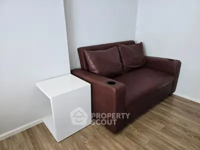 Modern living room with stylish brown leather sofa and sleek white side table on wooden flooring.