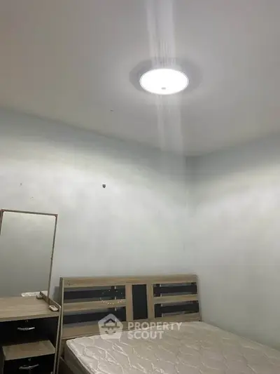 Minimalist bedroom with wooden bed frame and dresser, featuring a bright ceiling light.