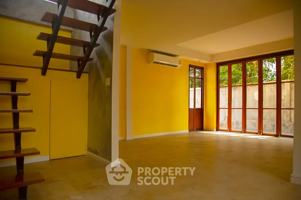 Bright living room with yellow walls, wooden staircase, and large windows.