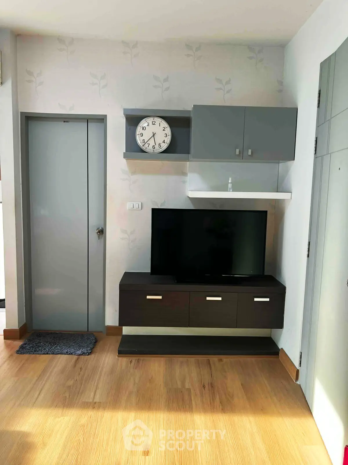 Modern living room with sleek TV unit and wall clock, featuring stylish wooden flooring and contemporary decor.