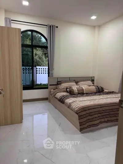 Cozy bedroom with modern decor and large window offering natural light and garden view.