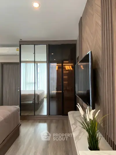 Modern bedroom with mirrored wardrobe and mounted TV, featuring elegant wood paneling and natural light.