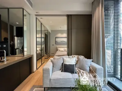 Chic modern living room seamlessly connected to a sleek kitchen, featuring plush sofa, elegant decor, and abundant natural light.