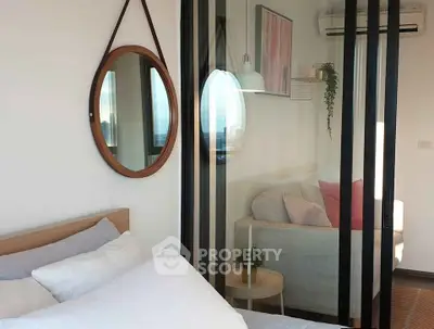 Modern bedroom with glass partition and cozy living area, featuring stylish decor and natural light.