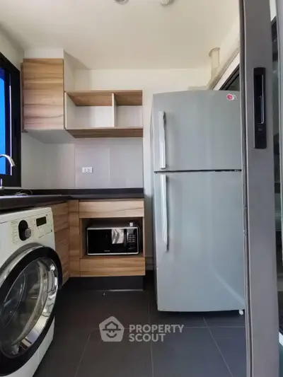 Modern kitchen with sleek appliances and wooden cabinetry, featuring a washing machine and large fridge.