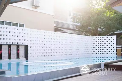 Modern outdoor pool with a stylish white perforated wall creating a private oasis in a serene courtyard setting, perfect for relaxation.