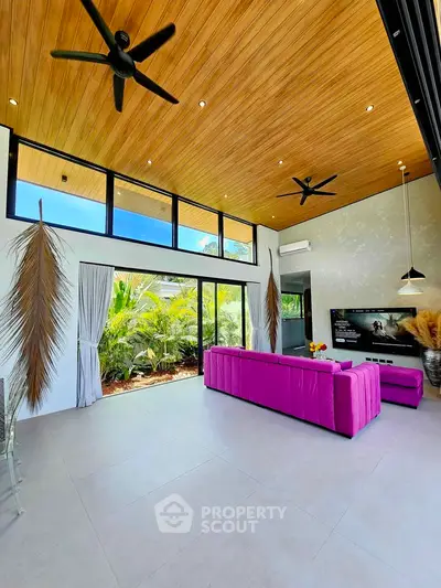 Spacious modern living room with high ceilings, vibrant pink sofa, and large windows overlooking lush greenery.