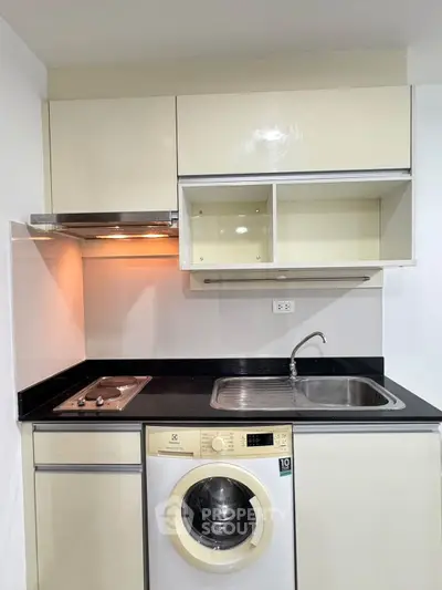 Modern compact kitchen with washing machine and electric stove in sleek apartment.