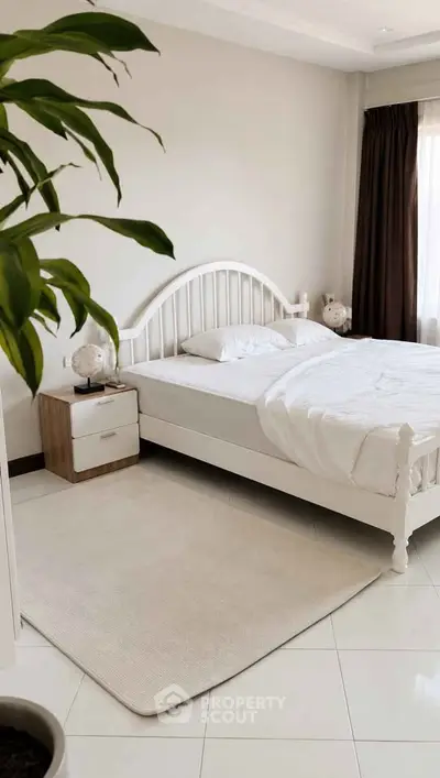 Cozy bedroom with white bed frame, nightstand, and large window for natural light.