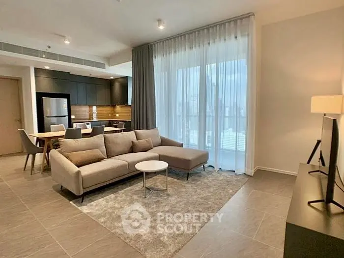 Modern living room with open kitchen and city view, featuring sleek furniture and natural light.