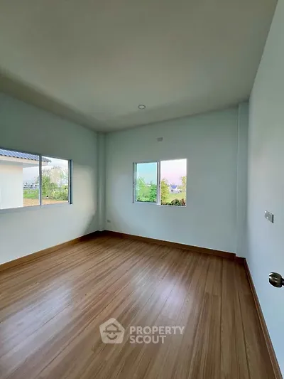 Spacious empty room with wooden flooring and large windows offering natural light.