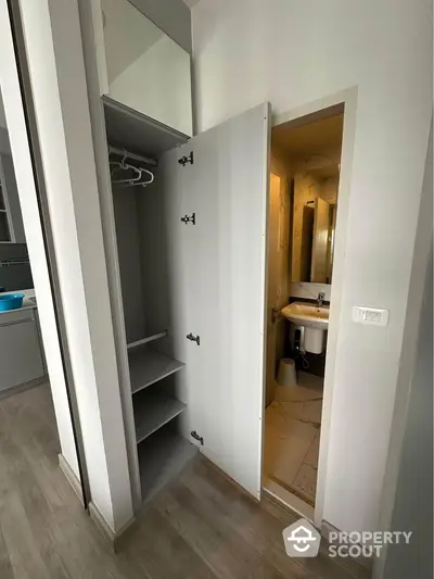 Modern apartment interior with open closet and bathroom view, featuring sleek design and neutral tones.