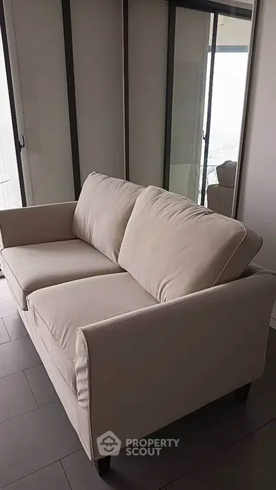 Modern beige sofa in a stylish living room with large windows and sleek flooring.