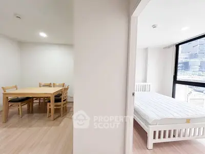 Modern apartment interior with dining area and bedroom, featuring large windows and natural light.