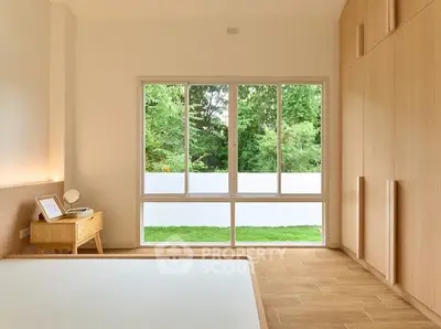 Spacious bedroom with large window and wooden flooring, overlooking lush greenery.