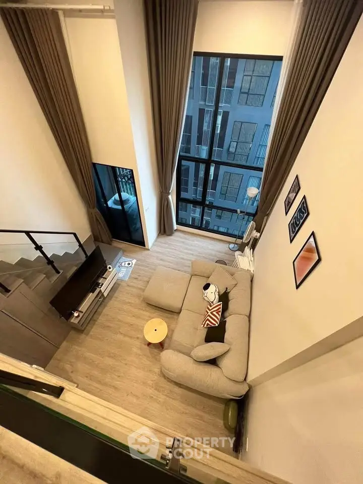 Modern loft-style living room with high ceilings and large windows offering a stunning city view.