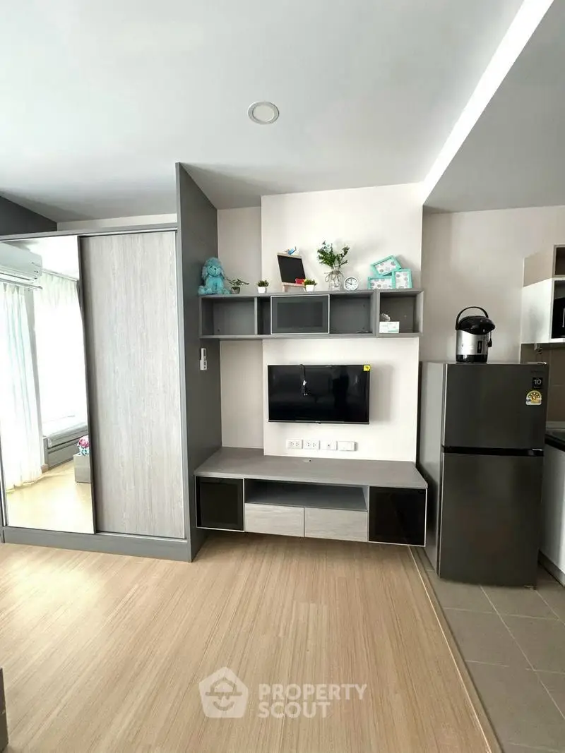 Modern living room with sleek TV unit and stainless steel fridge in a cozy apartment.