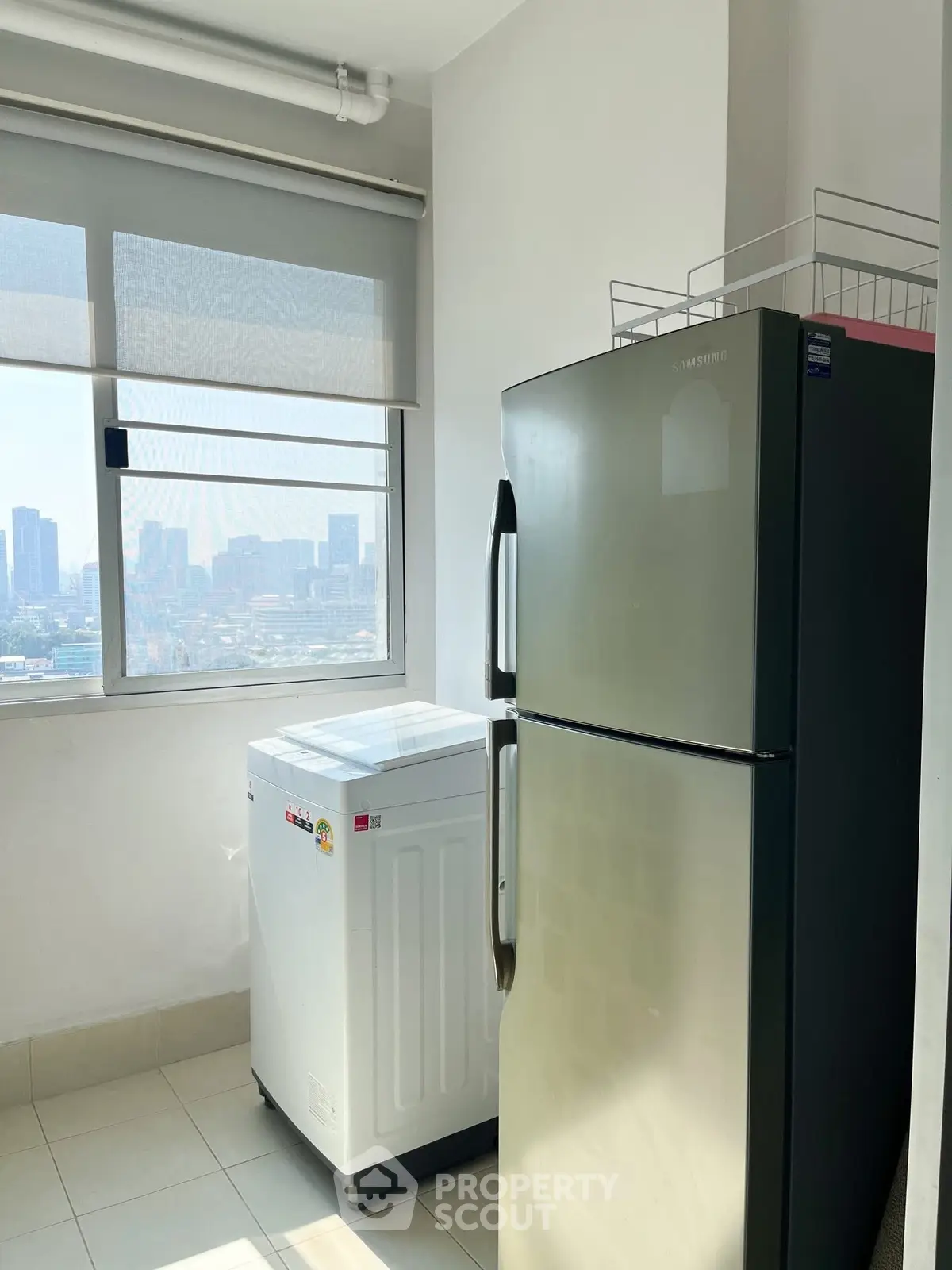 Bright utility room with modern fridge and washing machine, offering city views through large window.