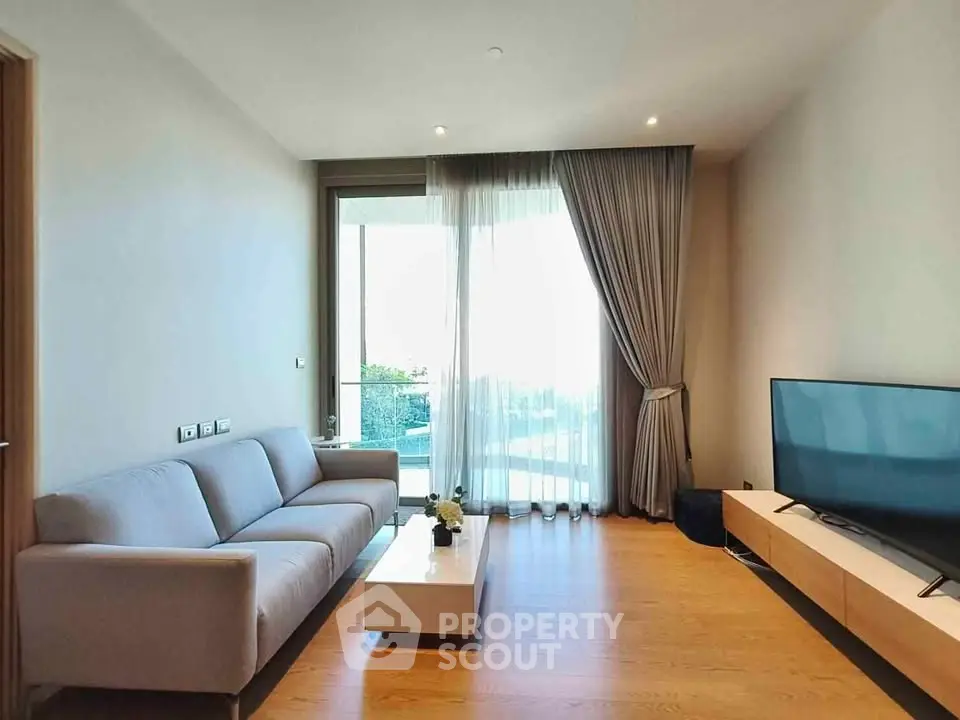 Modern living room with large TV and balcony view, featuring elegant decor and natural light.