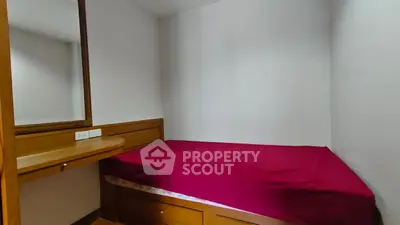 Cozy bedroom with built-in wooden furniture and red bedding, perfect for a compact living space.