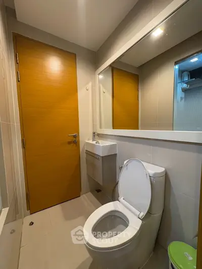 Modern bathroom with sleek design and wooden door, featuring a toilet and compact sink.