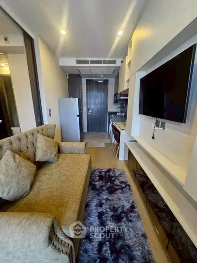 Modern living room with plush sofa, wall-mounted TV, and sleek kitchen area in a stylish apartment.
