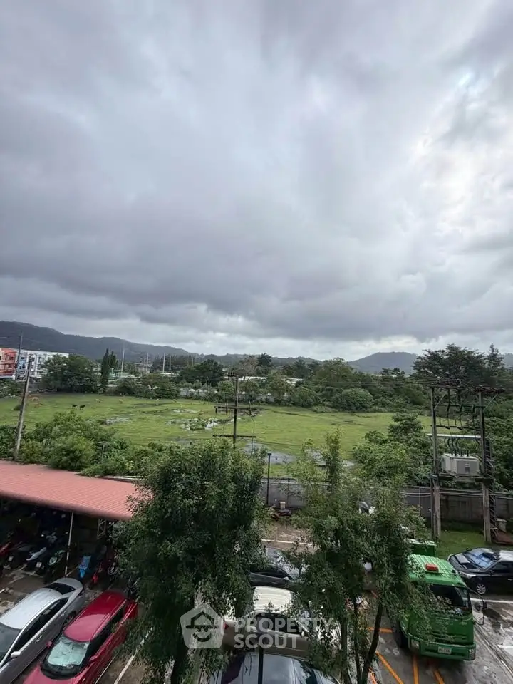 Scenic view of lush green landscape with parked cars and cloudy sky, ideal for real estate development.