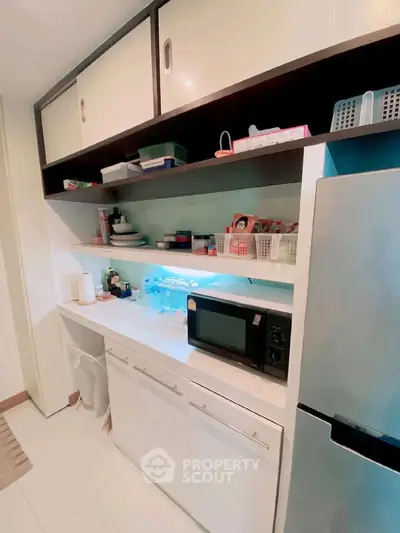 Modern kitchen with sleek cabinetry and stainless steel fridge, featuring a microwave and organized shelving.