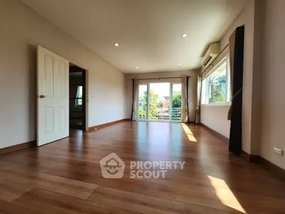 Spacious living room with wooden flooring and large windows offering natural light and garden view.