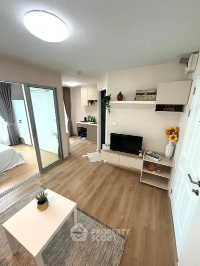Modern living room with stylish decor and wooden flooring, featuring a cozy TV area and sliding glass doors to bedroom.
