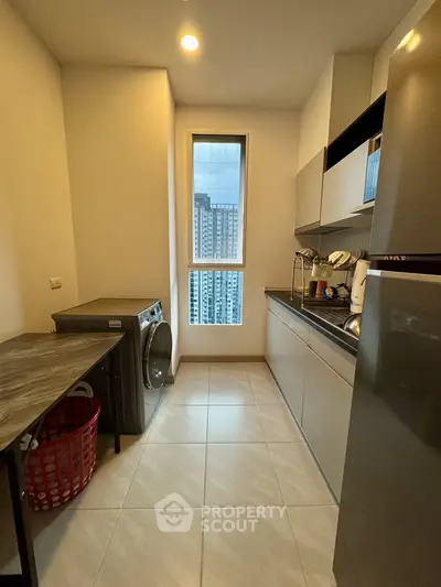 Modern kitchen with sleek cabinets, washing machine, and city view window.