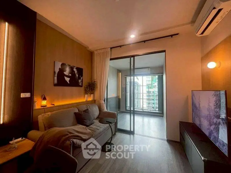 Modern living room with cozy sofa, large TV, and sliding glass doors leading to a balcony with city view.