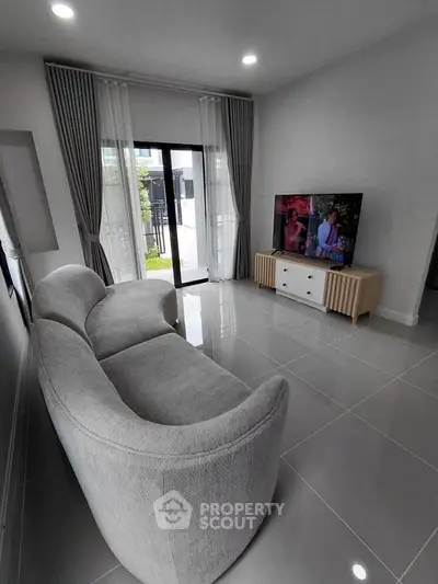 Modern living room with sleek gray sofa and large TV, featuring floor-to-ceiling windows and elegant curtains.
