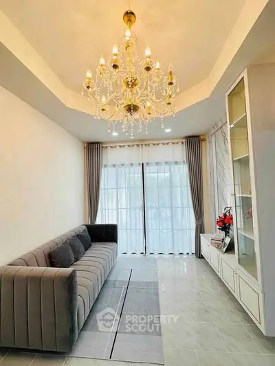 Elegant living room with chandelier and modern decor, featuring a plush sofa and large windows for natural light.