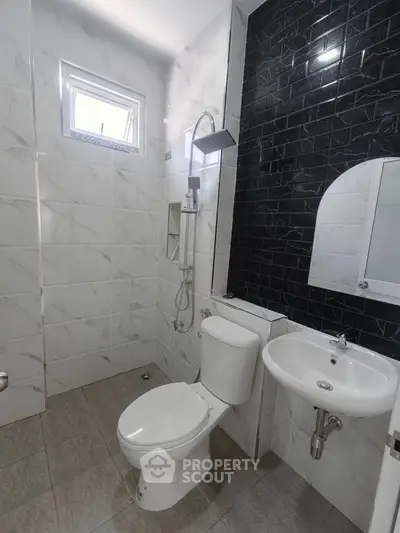 Modern bathroom with sleek black and white tiles, featuring a shower and compact fixtures.