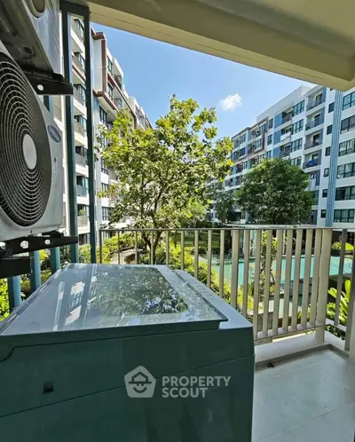 Modern apartment balcony with scenic view of lush garden and contemporary buildings.