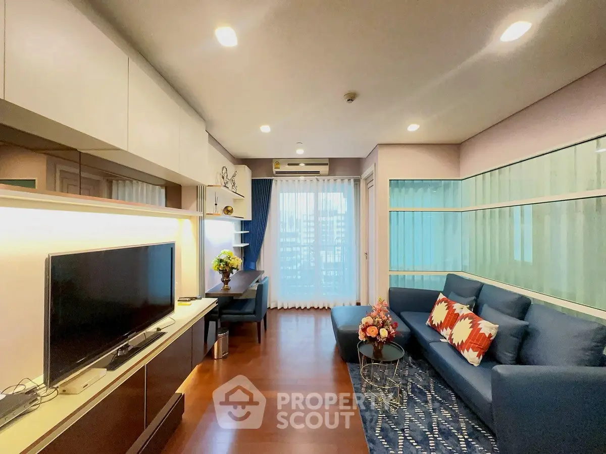 Modern living room with sleek design, featuring a blue sofa, TV, and large window with city view.