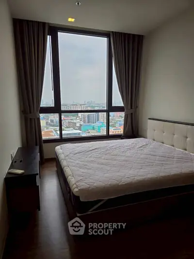 Cozy bedroom with large window offering stunning city views, perfect for urban living.
