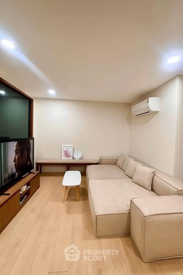 Modern living room with beige sectional sofa, wall-mounted TV, and air conditioning unit.