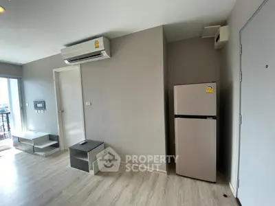 Modern apartment interior with air conditioning and fridge, featuring light wood flooring and neutral walls.
