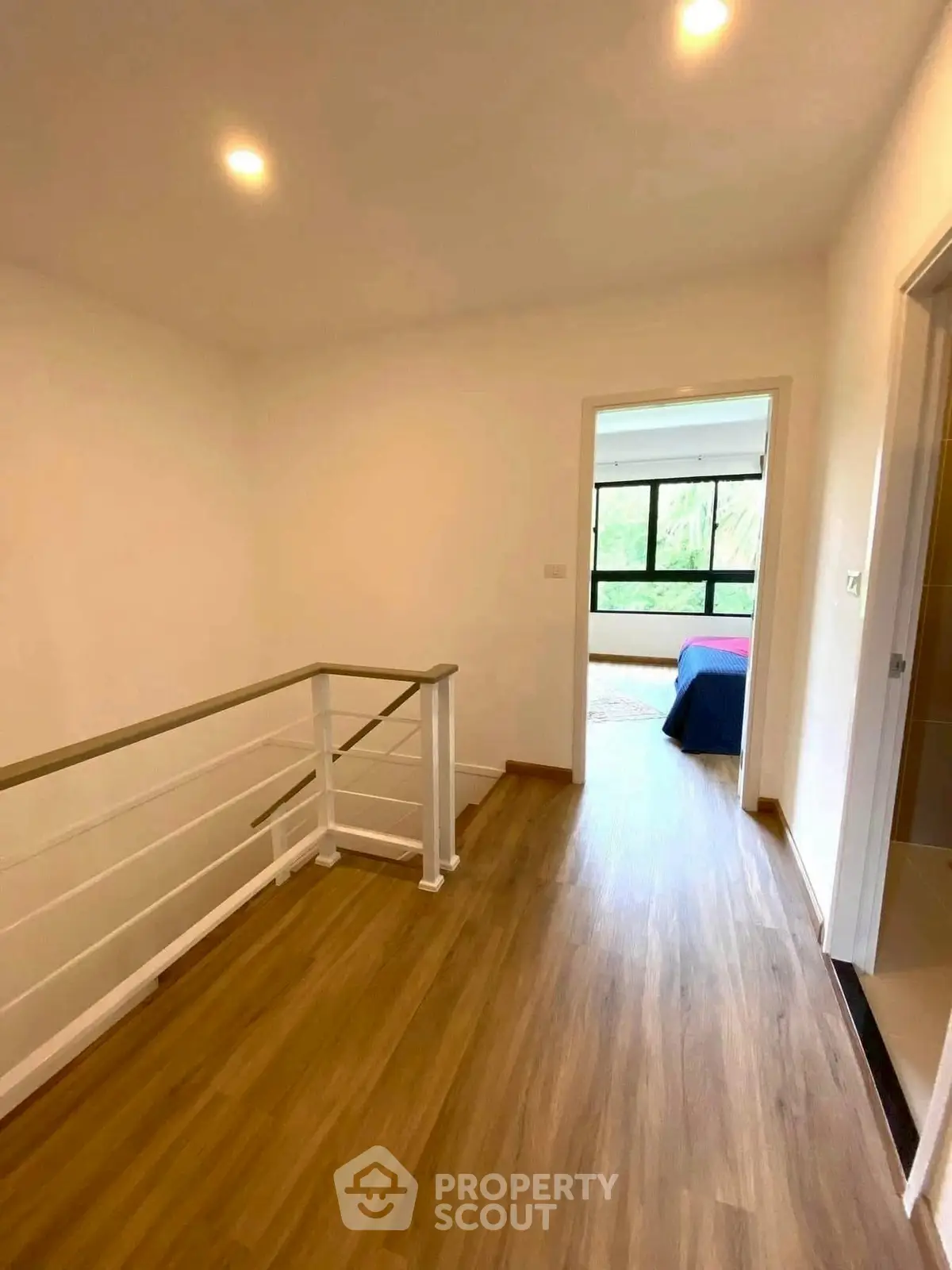 Bright hallway with wooden flooring leading to a bedroom with large window.