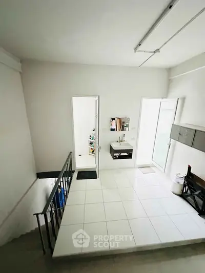 Spacious white-tiled room with staircase and open door, ideal for versatile use.