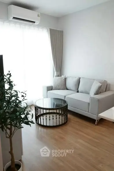 Modern living room with stylish sofa and glass coffee table, featuring natural light and wooden flooring.