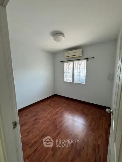 Spacious empty bedroom with wooden flooring and air conditioning, ready for customization.