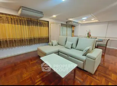 Spacious living room with elegant sofa and dining area, featuring wooden flooring and stylish decor.