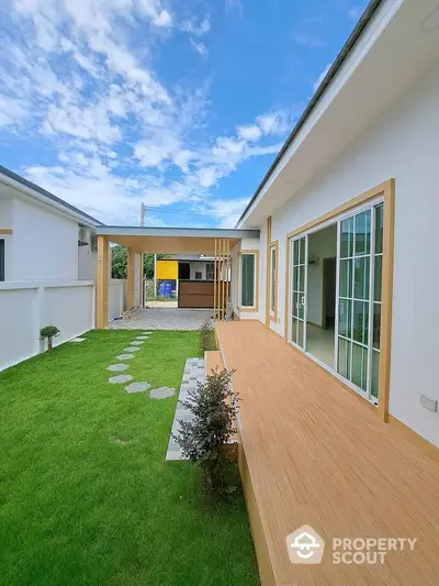 Modern home exterior with lush green lawn and wooden deck under a clear blue sky, featuring sliding glass doors.