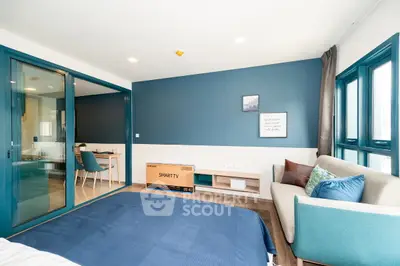 Modern bedroom with blue accents, smart TV, and cozy seating area in a stylish apartment.